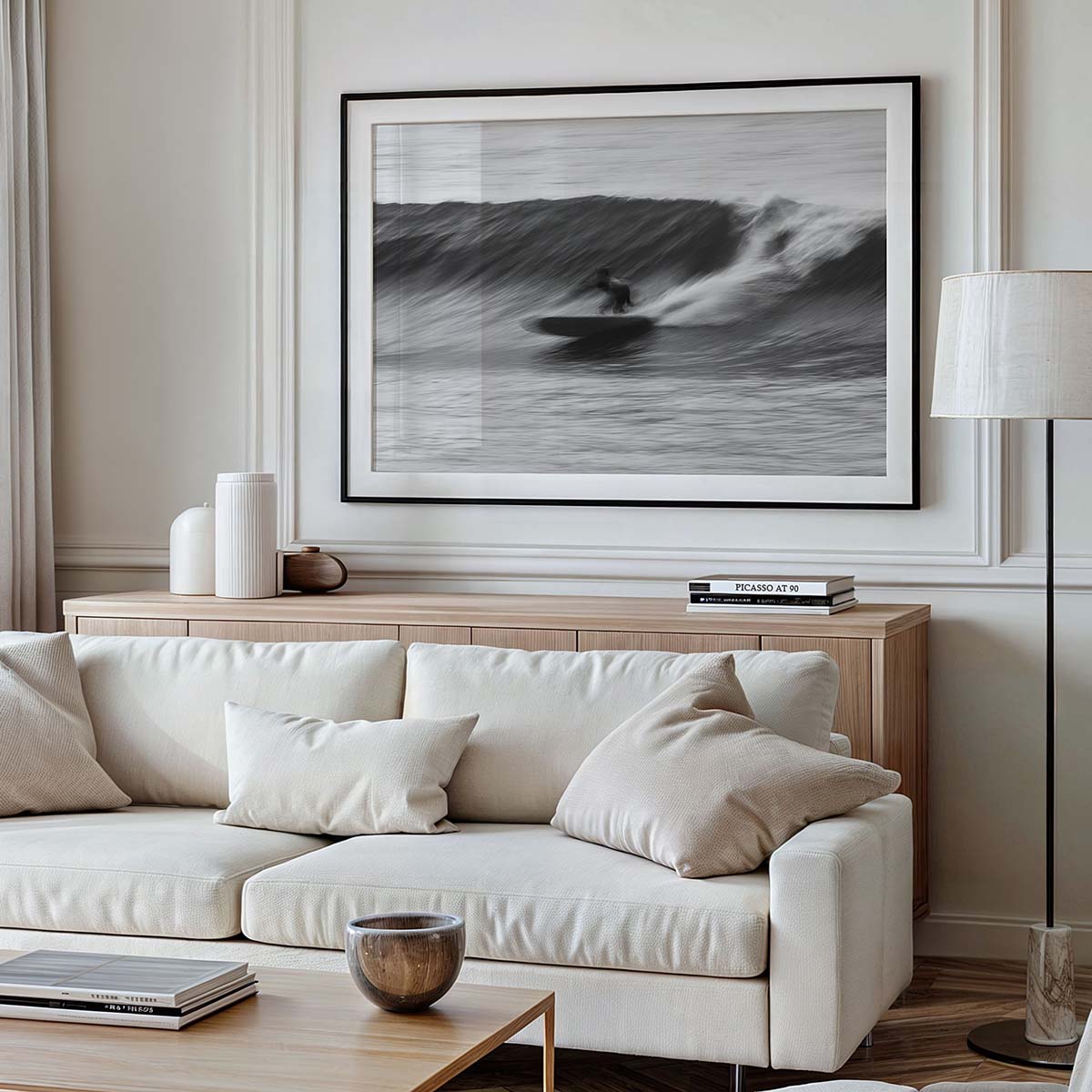 A framed black-and-white photograph of a surfer surfing a wave. The wall art hangs on a wall in a modern coastal-themed living room.