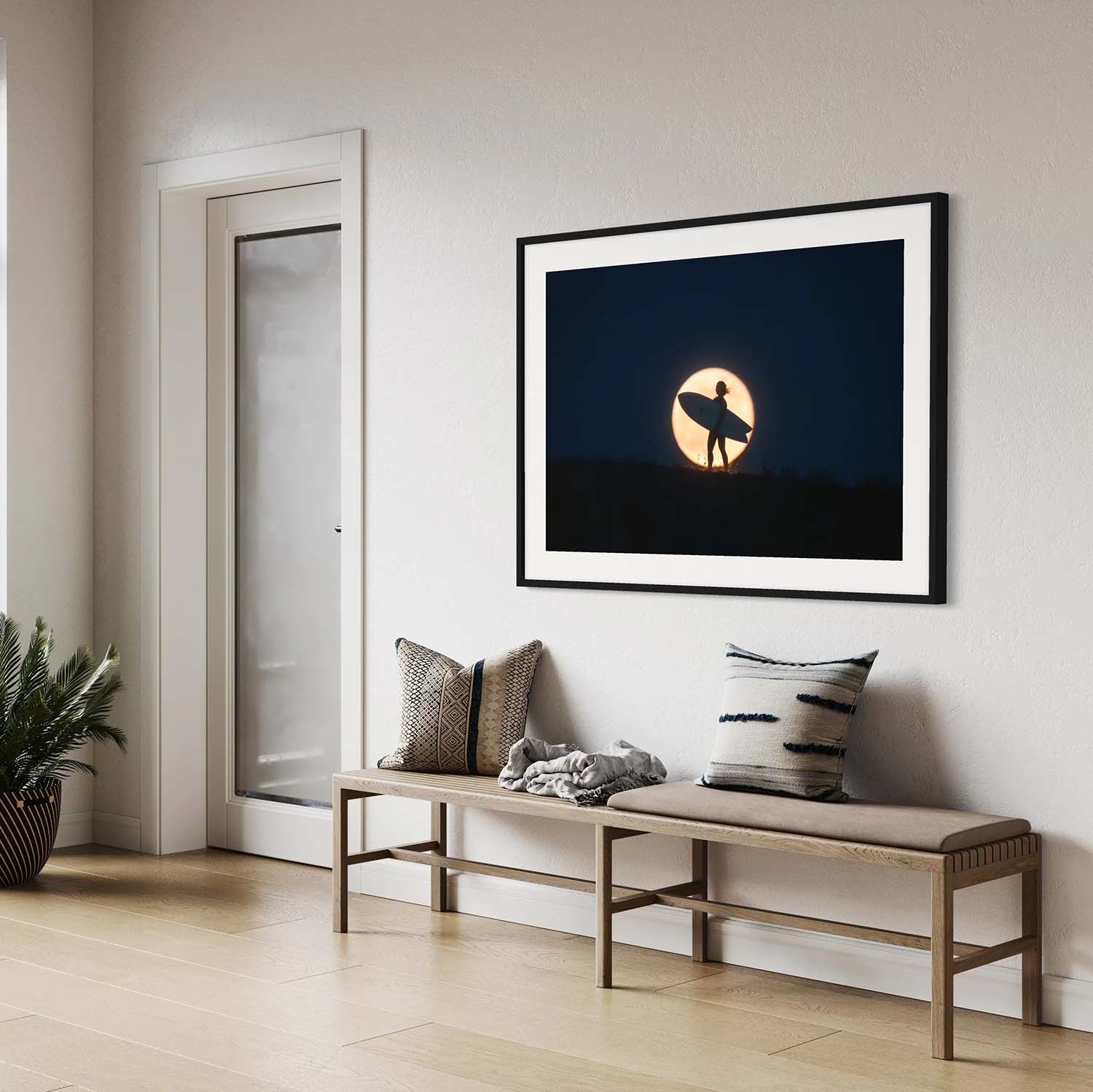 A photography print of a surfer standing against the backdrop of a full moon hanging in a mid-century modern entryway.