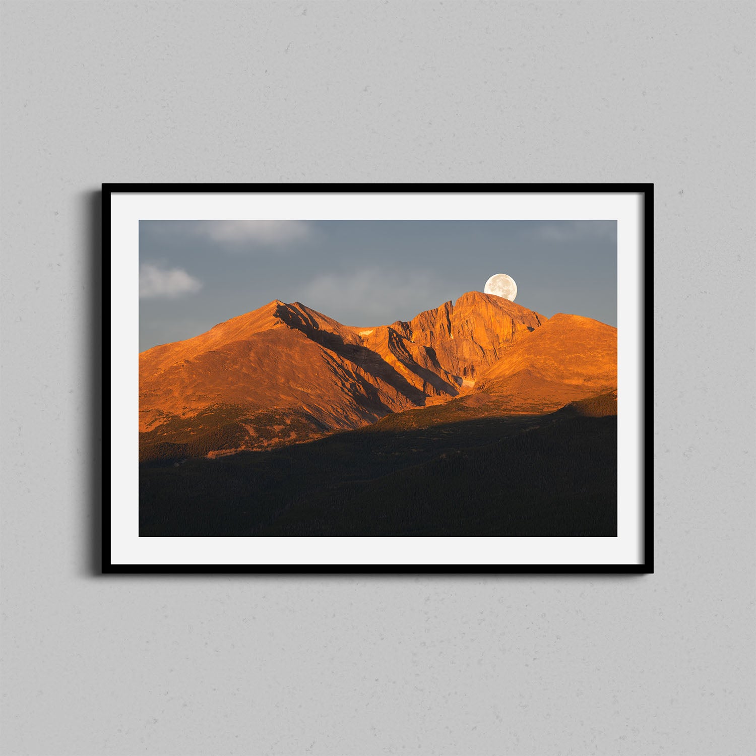 A fine art photography print of Colorado's Longs Peak at sunrise with the moon setting behind framed in a black wooden frame.