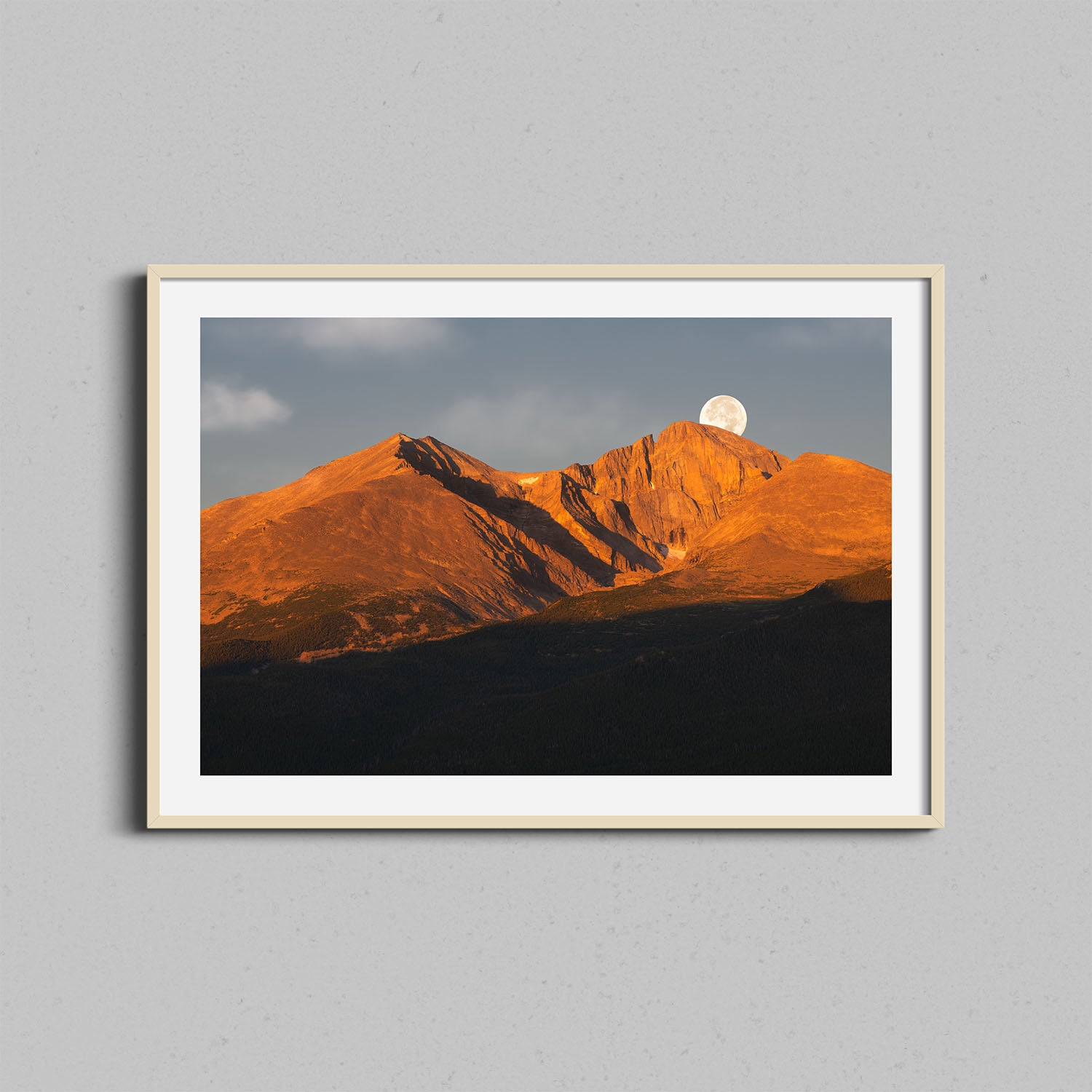 A photograph of Colorado's Longs Peak at sunrise with the moon setting behind framed in a natural wooden frame.