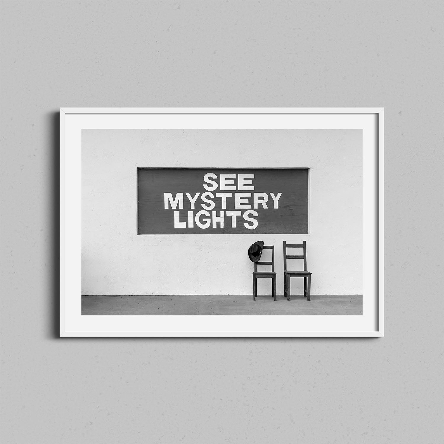 A black and white photography print of the See Mystery Lights sign in Marfa, Texas with a white wooden frame.