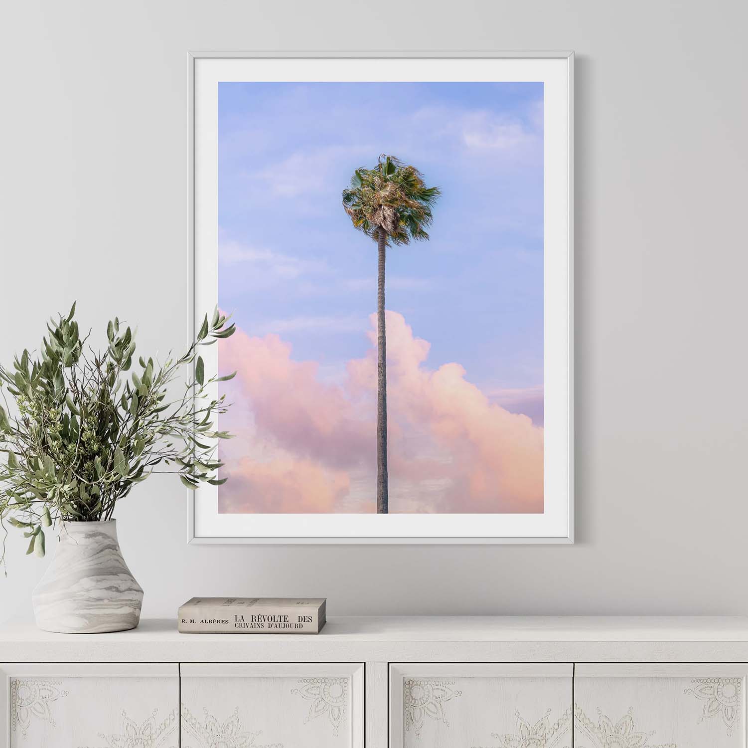 A framed photograph of a single palm tree against a sunset sky hanging on the wall in a modern entryway.
