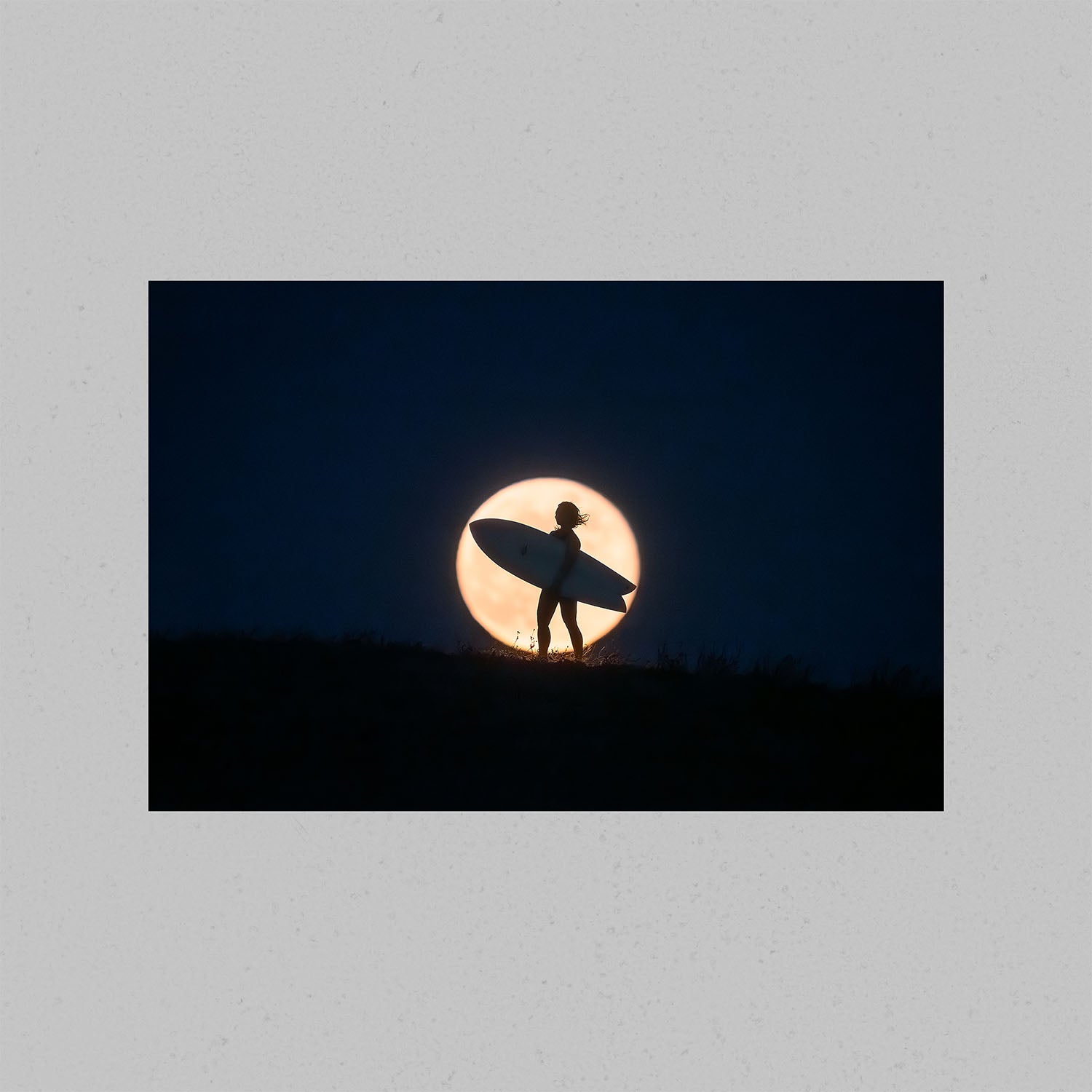 Wall art of a surfer holding a surfboard against the backdrop of a full moon.