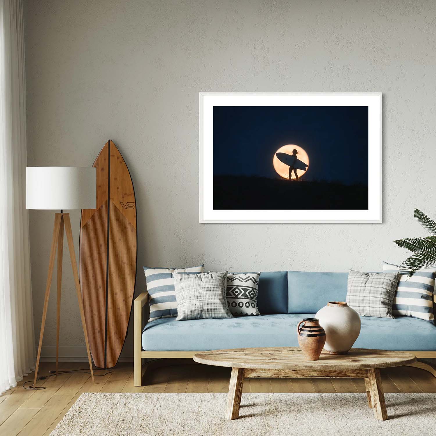 A photography print of a surfer standing against the backdrop of a full moon hanging in a coastal-inspired living room.