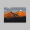 A photo of Colorado's Longs Peak at sunrise with the moon setting over the mountain.