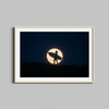 A surfer holds a surfboard against the backdrop of a full moon in this natural- framed photography print.